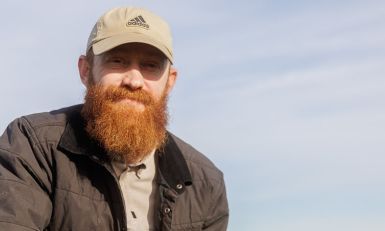 Farmer Mike smiles warmly while wearing a hat, standing outside.