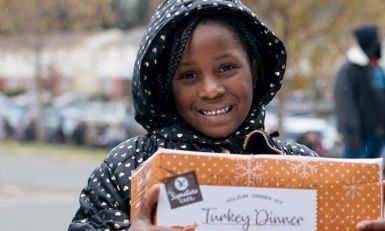 Alayaha in a polka dot coat holding a Thanksgiving Dinner box