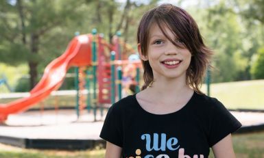 A girl smiling while standing in front of a playground.