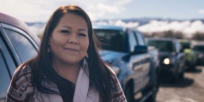 A woman smiling at the camera in front of a line of cars.