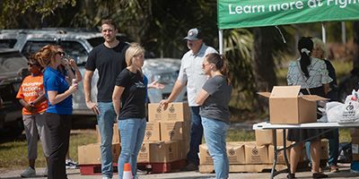 People standing next to food boxes and a tent.