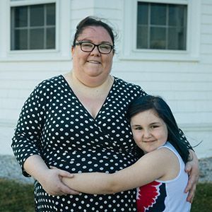 A daughter hugging her mother outside a house.