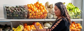 A woman holding an orange in front of fruit baskets.