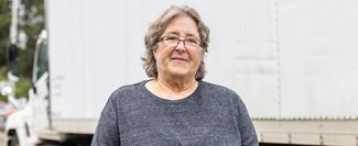 An older woman standing in front of a food delivery truck.